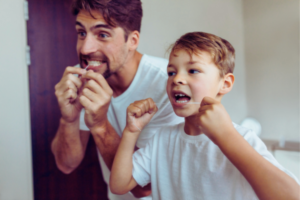 Padre e hijo usando hilo dental frente al espejo
