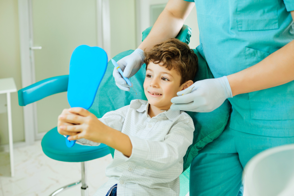 La primera visita al dentista: Una experiencia positiva para tu hijo Niño sonriendo mientras se mira en un espejo dental en la consulta del odontólogo pediátrico.